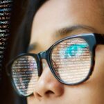 woman with glasses looking at a screen with code